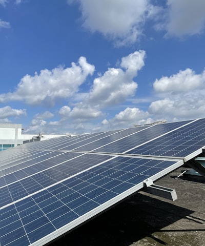 Solar panels are installed on a rooftop under a partly cloudy sky, capturing sunlight efficiently. The panels are aligned in neat rows, suggesting a modern approach to renewable energy.